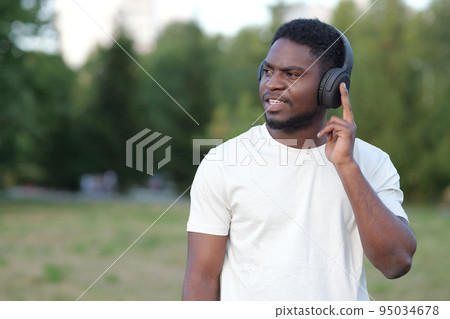 African American man listening to music walks in park 95034678