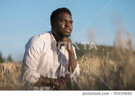 African American agriculturist sits on wheat field smiling African American agriculturist sits on wheat field smiling 95034680