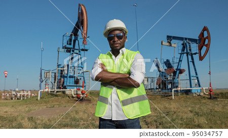 Black engineer stands against conventional pumping unit Black engineer stands against conventional pumping unit 95034757