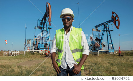 Black engineer stands against conventional pumping unit Black engineer stands against conventional pumping unit 95034761
