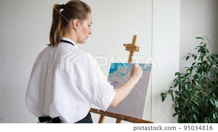 Mature woman artist paints sky landscape on easel canvas Mature woman artist paints sky landscape on easel canvas 95034816
