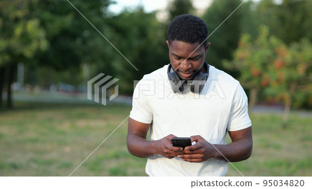 African American man walks typing messages on smartphone 95034820