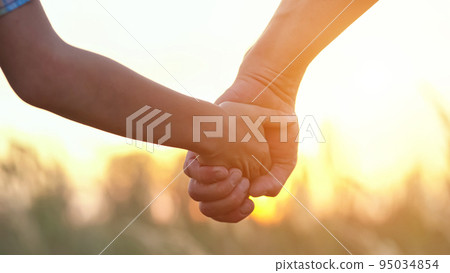 Son holds father hand against blurry sunset on evening sky 95034854