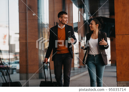 Business man and business woman talking and holding luggage traveling on a business trip, carrying fresh coffee in their hands.Business concept Business man and business woman talking and holding luggage traveling on a business trip, carrying fresh coffee in their hands.Business concept 95035714