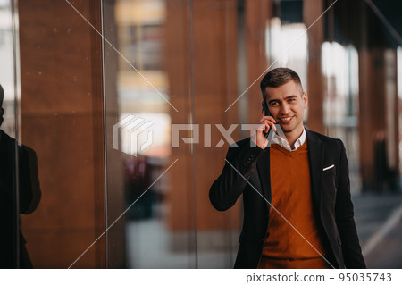 Going to airport terminal. Confident businessman traveler walking on city streets and pulling his suitcase drinking coffee and speaking on smartphone Going to airport terminal. Confident businessman traveler walking on city streets and pulling his suitcase drinking coffee and speaking on smartphone 95035743