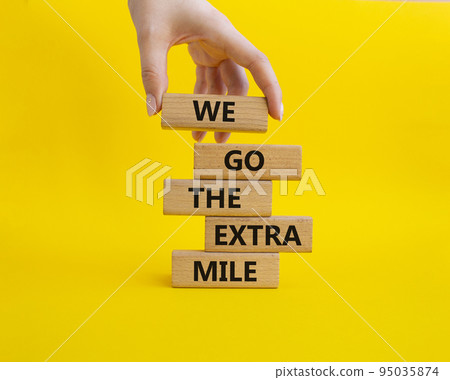 We go the extra mile symbol. Wooden blocks with words 'We go the extra mile'. Beautiful yellow background. Businessman hand. Business and 'We go the extra mile' concept. Copy space. 95035874