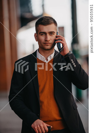Going to airport terminal. Confident businessman traveler walking on city streets and pulling his suitcase drinking coffee and speaking on smartphone 95035931