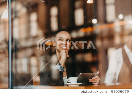woman in a coffee shop drink coffee viewed through glass with reflections as they sit at a table chatting and laughing woman in a coffee shop drink coffee viewed through glass with reflections as they sit at a table chatting and laughing 95036079