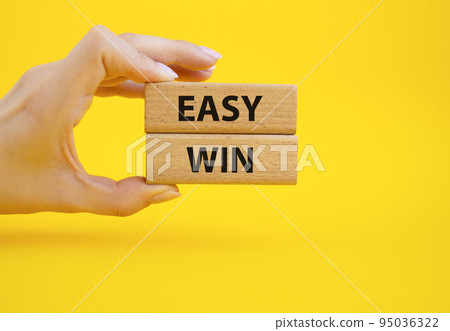 Easy win symbol. Wooden blocks with words Easy win. Beautiful yellow background. Businessman hand. Business and Easy win concept. Copy space. 95036322
