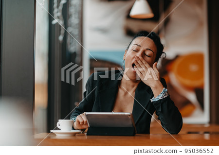A sleepy woman sits in a cafe during a break and uses a tablet.Business concept. A sleepy woman sits in a cafe during a break and uses a tablet.Business concept. 95036552