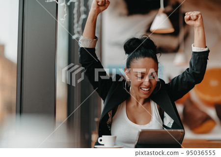 A woman sits in a cafe with her arms raised and celebrating a job well done.Business concept A woman sits in a cafe with her arms raised and celebrating a job well done.Business concept 95036555