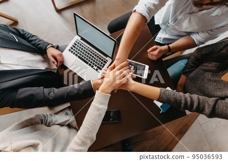 Top view of business people in formal wear sitting coffee and analyzing data. On desk are laptops, graphs, tablets and paperwork. 95036593