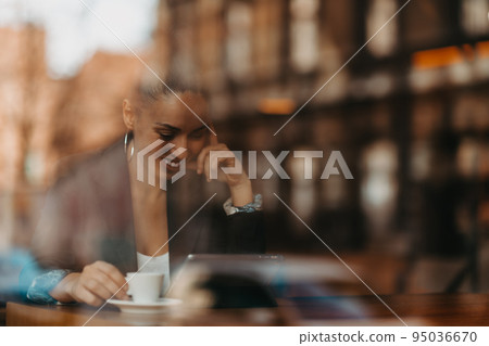 woman in a coffee shop drink coffee viewed through glass with reflections as they sit at a table chatting and laughing woman in a coffee shop drink coffee viewed through glass with reflections as they sit at a table chatting and laughing 95036670