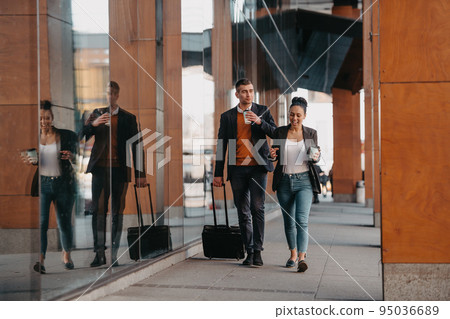 Business man and business woman talking and holding luggage traveling on a business trip, carrying fresh coffee in their hands.Business concept 95036689