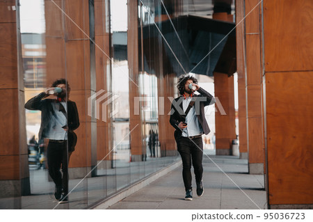 Trendy businessman with leather briefcase in financial district using smartphone while listening audio songs headphones drinking coffee Trendy businessman with leather briefcase in financial district using smartphone while listening audio songs headphones drinking coffee 95036723