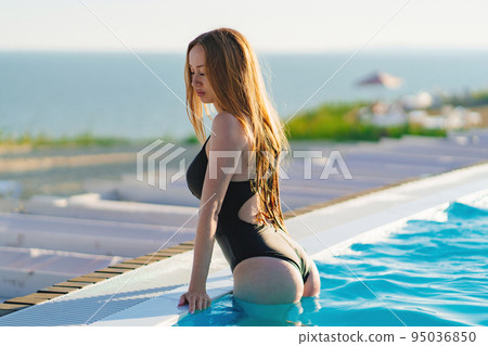 A happy beautiful woman in a black swimsuit by the side of a pool. A happy beautiful woman in a black swimsuit by the side of a pool. 95036850