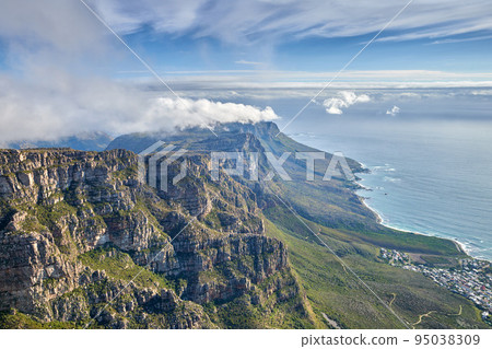 Aerial view of mountain and calm ocean with a blue cloudy sky background and copy space. Stunning nature landscape of the sea and horizon from Table Mountain with beautiful greenery in Cape Town 95038309