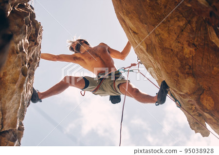 Fitness, rock climbing and strong mountain climber on a cliff with ropes in summer challenge and extreme exercise. Danger, courage and healthy man fearless, sports and big rocks or stone below view 95038928