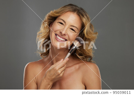 Beauty, makeup skincare with a happy senior model holding a cosmetic brush in studio against a grey background. Portrait of an elderly woman with a smile posing for wellness, healthcare and cosmetics Beauty, makeup skincare with a happy senior model holding a cosmetic brush in studio against a grey background. Portrait of an elderly woman with a smile posing for wellness, healthcare and cosmetics 95039011