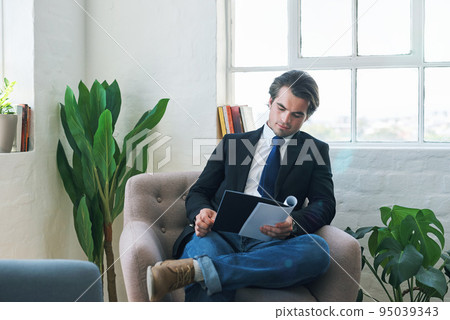Young businessman reading paperwork, on couch at home and looking at financial analysis document for career development. Business finance report, changes in economy and success with accounting audit Young businessman reading paperwork, on couch at home and looking at financial analysis document for career development. Business finance report, changes in economy and success with accounting audit 95039343