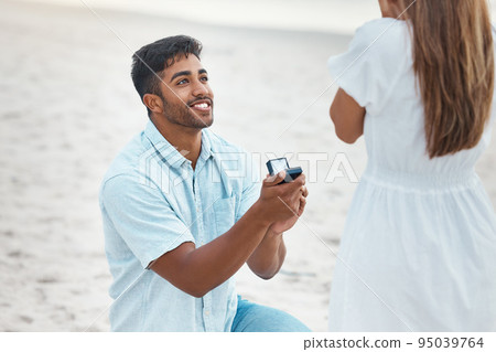 Proposal, surprise and engagement with wedding ring on beach with indian man on knee for love, commitment and marriage. Save the date, gift and diamond jewellery present for woman for romance Proposal, surprise and engagement with wedding ring on beach with indian man on knee for love, commitment and marriage. Save the date, gift and diamond jewellery present for woman for romance 95039764