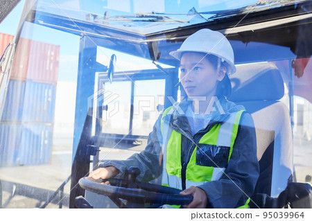 Asian woman, logistics and machine for industry shipping at work for transportation in container yard. An engineer working in industrial warehouse with transport machinery for cargo shipment 95039964