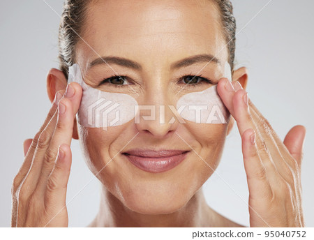 Eye wellness, skincare and mature woman with dermatology product for face against a grey studio background. Portrait of an elderly spa model with patch cosmetics for eyes for clean facial skin 95040752