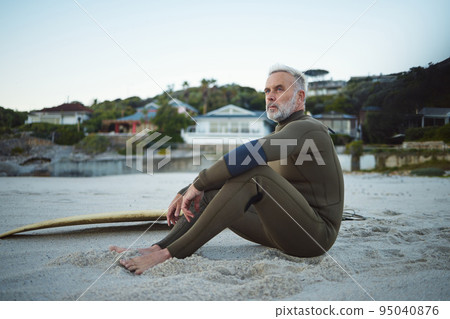 Thinking, relax and surfer man on the beach for rest, peace and freedom while on tropical holiday. Thoughtful, retirement and senior man sitting on sand in nature by the ocean during surf training. 95040876