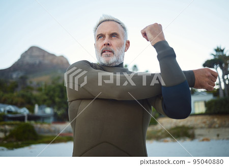 Fitness, surf and stretching with a sports man getting ready for a workout, exercise or training outdoor at the beach. Health, wellness and performance with a mature male at the start of his routine 95040880