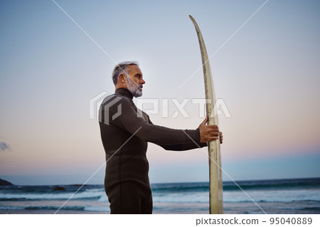 Surfer, surfboard and senior man at the beach during sunset after surfing on the waves in the sea water. Elderly male on a surf travel vacation in hawaii to enjoy sport, hobby and tropical weather Surfer, surfboard and senior man at the beach during sunset after surfing on the waves in the sea water. Elderly male on a surf travel vacation in hawaii to enjoy sport, hobby and tropical weather 95040889