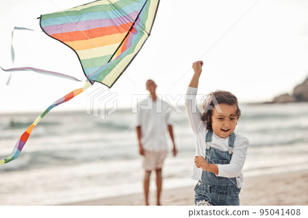 Family, beach and kite with child running for summer holiday, happiness and childhood while father watches. Happy, youth and childhood with young girl playing with colorful toy at seaside vacation 95041408