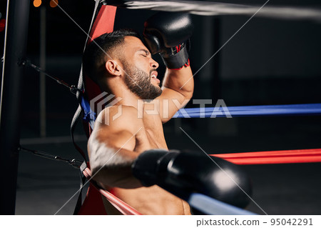Tired boxer, fitness and sports competition in boxing ring, relax during mma fight and breathing after wellness exercise training at gym. Frustrated Muay Thai athlete without energy for workout Tired boxer, fitness and sports competition in boxing ring, relax during mma fight and breathing after wellness exercise training at gym. Frustrated Muay Thai athlete without energy for workout 95042291