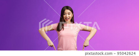 Lively enthusiastic asian brunette female excited telling about awesome promo, pointing down surprised, grinning joyfully recommend good advertisement, indicating bottom advertisement 95042624