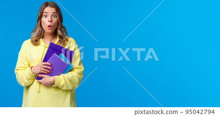 Waist-up portrait of surprised and wondered blonde caucasian female say wow and express amazement hear interesting news, gossiping in college, holding notebooks and essay, blue background Waist-up portrait of surprised and wondered blonde caucasian female say wow and express amazement hear interesting news, gossiping in college, holding notebooks and essay, blue background 95042794