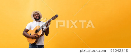 Muscular black man playing guitar, wearing jeans and white tank-top. Isolate over yellow background. Muscular black man playing guitar, wearing jeans and white tank-top. Isolate over yellow background. 95042848