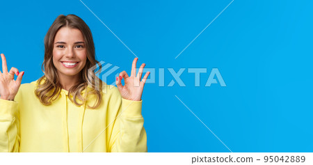 Close-up portrait happy confident young blond girl assure all okay, guarantee plan went well, smiling and show ok gesture in approval, confirmation or like, stand blue background Close-up portrait happy confident young blond girl assure all okay, guarantee plan went well, smiling and show ok gesture in approval, confirmation or like, stand blue background 95042889