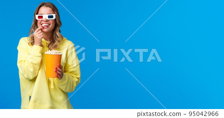 Leisure, fun and youth concept. Happy entertained smiling blond girl in 3d glasses, eating popcorn and laughing as watching funny comedy, go cinema watch movie with friends, blue backgorund Leisure, fun and youth concept. Happy entertained smiling blond girl in 3d glasses, eating popcorn and laughing as watching funny comedy, go cinema watch movie with friends, blue backgorund 95042966