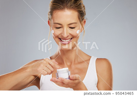 Mature model, skincare and cream on face for health, beauty and happy in cosmetics studio. Woman, skin and luxury anti-aging product in jar for facial, happiness and wellness with dark background 95043465