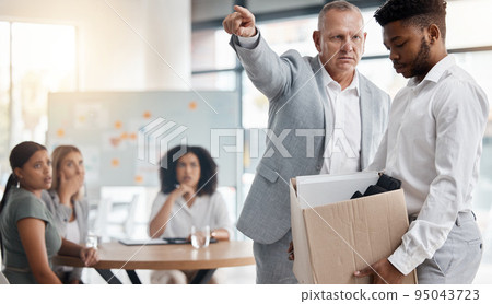 Black man, sad and fired by boss in a meeting holding a box in disappointment at the office. Manager or company leader pointing to the exit and firing employee in front of colleagues at the workplace 95043723