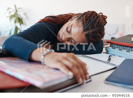 Tired student sleeping at her desk while studying for university or college exams and test. Burnout young woman lying on desk, fatigue or sleep during study session in her living room at home 95044016