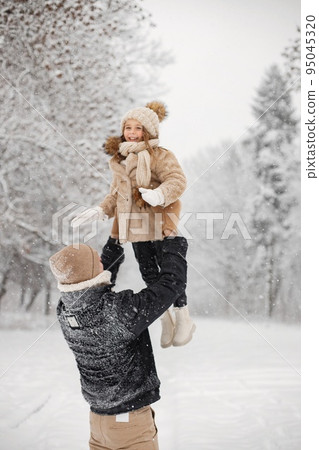 Little girl and her father playing outdoors at winter day. Man holding his daughter in the air. Father and daughter wearing winter clothes and knitted hats. Little girl and her father playing outdoors at winter day. Man holding his daughter in the air. Father and daughter wearing winter clothes and knitted hats. 95045320