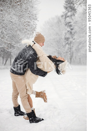 Young man and woman hugging and kissing outdoors. Romantic couple at winter in warm jackets walk in the park and hugging. Man and woman wearing winter clothes and knitted hats. Young man and woman hugging and kissing outdoors. Romantic couple at winter in warm jackets walk in the park and hugging. Man and woman wearing winter clothes and knitted hats. 95045363