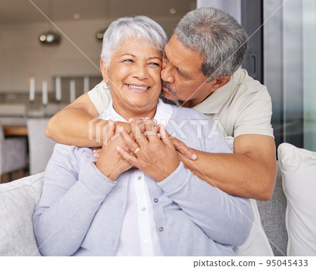 Happy senior couple kiss on sofa and smile for love, happiness and trust in family home or house living room. Elderly Mexico man and woman or people in retirement hug, kissing and romance on couch Happy senior couple kiss on sofa and smile for love, happiness and trust in family home or house living room. Elderly Mexico man and woman or people in retirement hug, kissing and romance on couch 95045433