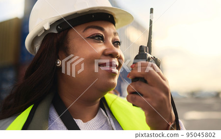 Logistics, delivery and black woman in communication via radio for manufacturing supply chain about shipping. Smile, engineer and happy manager in conversation with distribution worker at a port Logistics, delivery and black woman in communication via radio for manufacturing supply chain about shipping. Smile, engineer and happy manager in conversation with distribution worker at a port 95045802