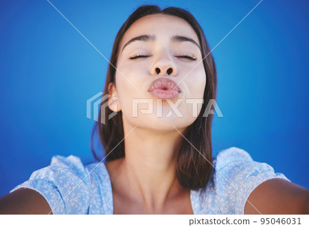 Woman face, blowing kiss and selfie portrait blue background for love emoji, relax and flirting on social media. Young girl beauty lips, mouth and funny expression of joy, happiness or summer style Woman face, blowing kiss and selfie portrait blue background for love emoji, relax and flirting on social media. Young girl beauty lips, mouth and funny expression of joy, happiness or summer style 95046031