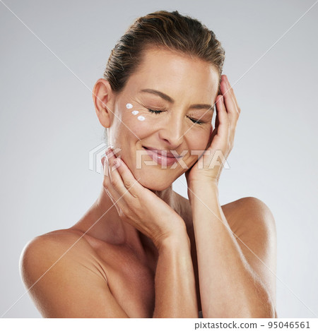 Mature skincare, beauty routine and using cream on face with a healthy cosmetic anti aging moisturizer. Portrait of health self care, with facial eye lotion and smile in grey studio mockup background 95046561