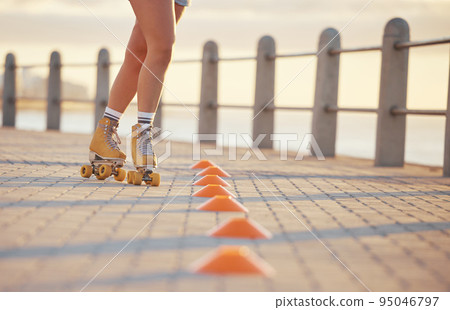 Woman roller skating with fitness cones outdoor on the promenade at the beach during summer. Girl practicing her skating skill while training for a sports activity in nature at the ocean. Woman roller skating with fitness cones outdoor on the promenade at the beach during summer. Girl practicing her skating skill while training for a sports activity in nature at the ocean. 95046797