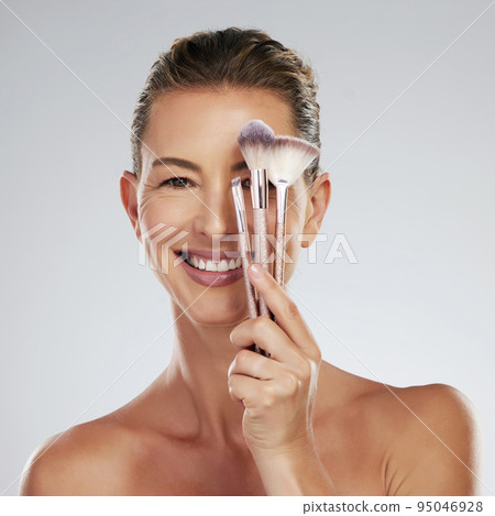 Mature, model and brush for makeup in hand by face with happiness for cosmetic, beauty or skincare portrait. Woman, smile and powder happy against studio backdrop for skin health, care and wellness Mature, model and brush for makeup in hand by face with happiness for cosmetic, beauty or skincare portrait. Woman, smile and powder happy against studio backdrop for skin health, care and wellness 95046928
