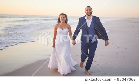 Wedding, couple and beach with a man and woman holding hands while walking on the sand by the ocean or sea. Love, trust and marriage with a bride and groom on the coast at sunset for celebration Wedding, couple and beach with a man and woman holding hands while walking on the sand by the ocean or sea. Love, trust and marriage with a bride and groom on the coast at sunset for celebration 95047062