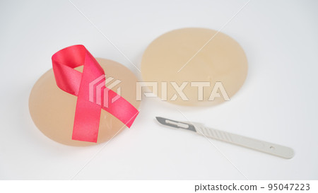 Breast silicone implants, pink tape and a disposable scalpel on a white background. Breast silicone implants, pink tape and a disposable scalpel on a white background. 95047223